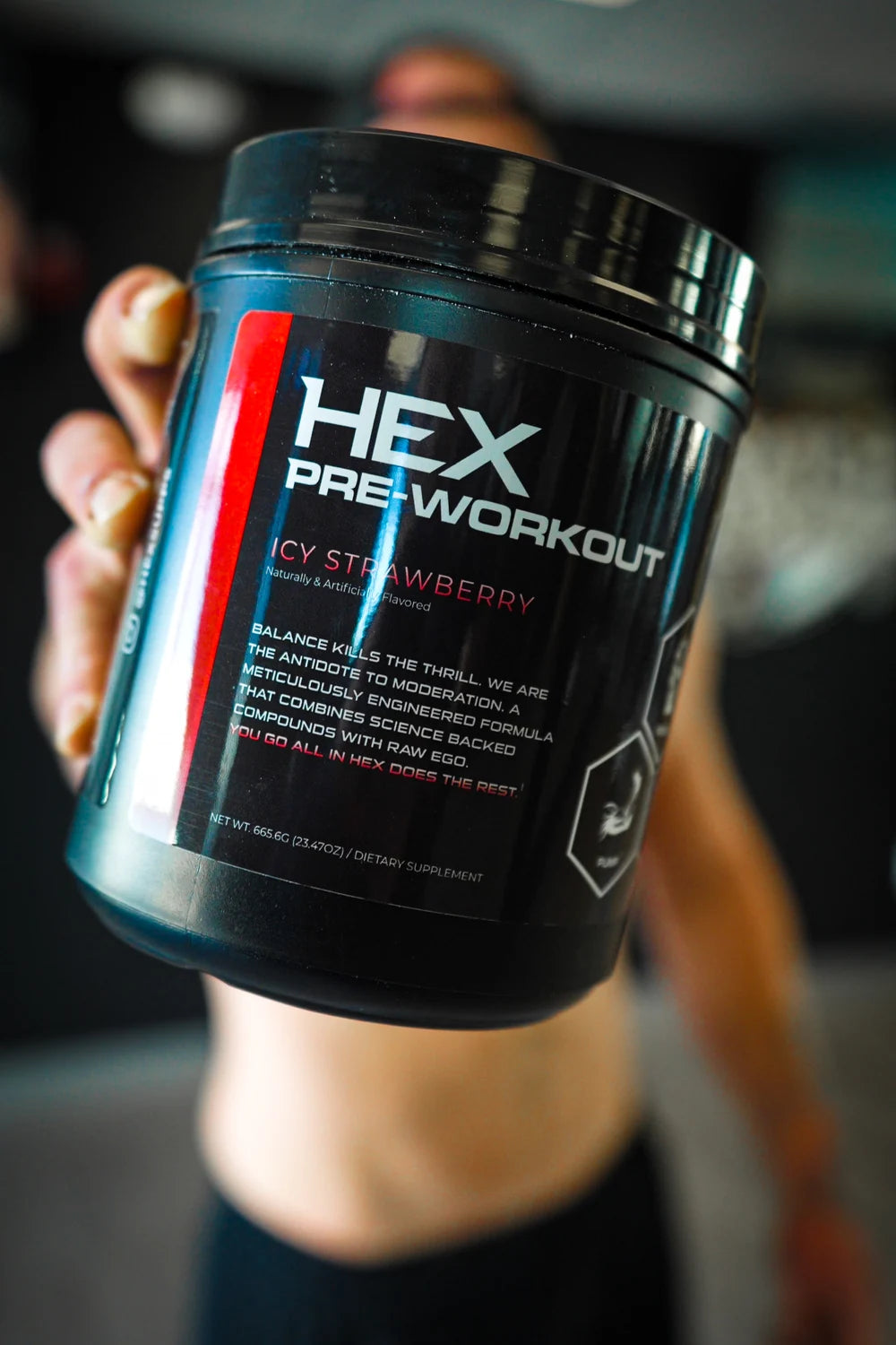 HEX Icy Strawberry pre-workout tub held toward the camera at the gym.