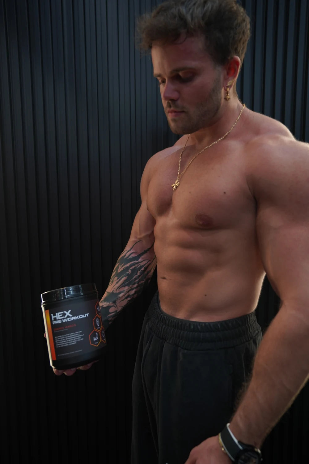 Athlete holding HEX Orange Mango pre-workout against a dark wall.